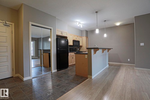 Kitchen featuring light wood-finish cabinetry, dark countertops, black appliances, and pendant lighting over a peninsula - #209 304 Ambleside Link Li Sw Sw, Edmonton, AB - Indoor Photo Showing Kitchen