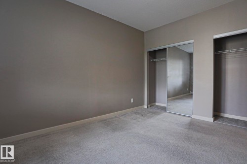 Neutral tone wall paint, light-toned carpet flooring, mirrored closet doors, and wire shelving - #209 304 Ambleside Link Li Sw Sw, Edmonton, AB - Indoor Photo Showing Other Room
