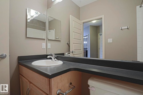 Vanity with an integrated sink, dark countertop, wood-finish cabinetry, and chrome fixtures - #209 304 Ambleside Link Li Sw Sw, Edmonton, AB - Indoor Photo Showing Bathroom