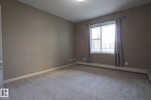 Carpeted flooring, neutral wall tones, white window trim, and baseboard heating - #209 304 Ambleside Link Li Sw Sw, Edmonton, AB - Indoor Photo Showing Other Room