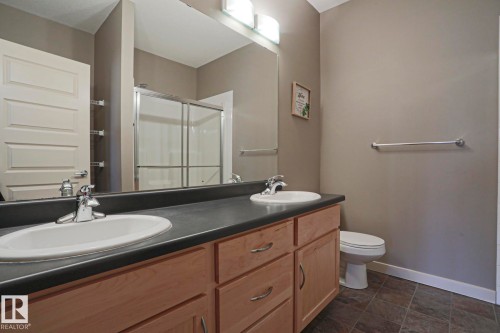 Double vanity with wood-finish cabinetry, integrated sinks, and a dark countertop - #209 304 Ambleside Link Li Sw Sw, Edmonton, AB - Indoor Photo Showing Bathroom