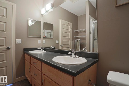 Dual vanity with a dark countertop and undermount sinks - #209 304 Ambleside Link Li Sw Sw, Edmonton, AB - Indoor Photo Showing Bathroom
