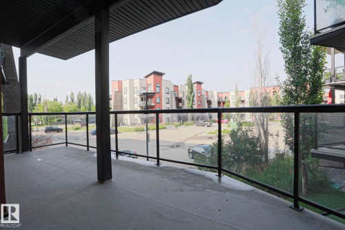 Concrete patio with black metal and glass railing, featuring an overhead balcony - #209 304 Ambleside Link Li Sw Sw, Edmonton, AB - Outdoor With Balcony With Exterior