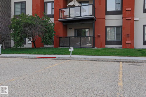 Ground-level patio with black railing, upper balcony with glass panel railing, and exterior facade with red accents - #209 304 Ambleside Link Li Sw Sw, Edmonton, AB - Outdoor With Balcony