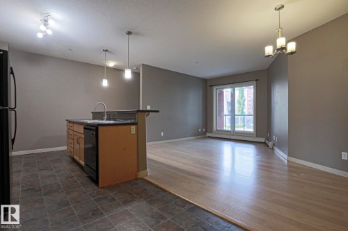 Kitchen island with integrated sink, black dishwasher, and pendant lighting - #209 304 Ambleside Link Li Sw Sw, Edmonton, AB - Indoor