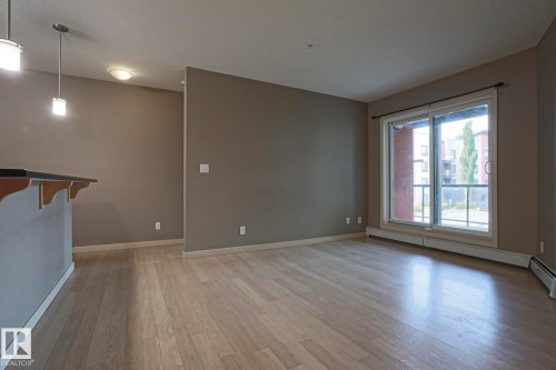 Wood-finish flooring, sliding glass door, pendant lighting, and built-in breakfast bar - #209 304 Ambleside Link Li Sw Sw, Edmonton, AB - Indoor Photo Showing Other Room