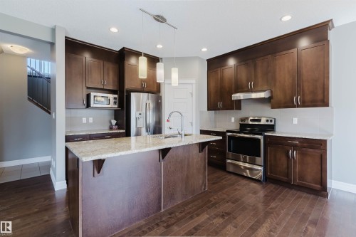 Kitchen featuring dark wood-finish cabinetry, light-toned countertops, stainless steel appliances, and wood-finish flooring - 15839 10 Avenue Sw, Edmonton, AB - Indoor Photo Showing Kitchen With Stainless Steel Kitchen With Upgraded Kitchen