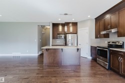 Kitchen featuring wood-finish flooring, dark wood cabinetry, stainless steel appliances, a center island with pendant lighting, and light-colored countertops - 
