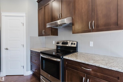 Rich wood-finish cabinetry, stainless steel range and hood, light-toned countertop, square tile backsplash, and five-panel interior door - 15839 10 Avenue Sw, Edmonton, AB - Indoor Photo Showing Kitchen With Upgraded Kitchen
