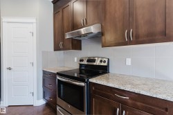 Rich wood-finish cabinetry, stainless steel range and hood, light-toned countertop, square tile backsplash, and five-panel interior door - 