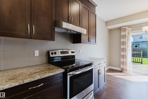 Rich wood-finish cabinetry with stainless steel hardware, durable tile backsplash, granite-style countertops, stainless steel appliances, and wood-finish flooring - 15839 10 Avenue Sw, Edmonton, AB - Indoor Photo Showing Kitchen With Stainless Steel Kitchen