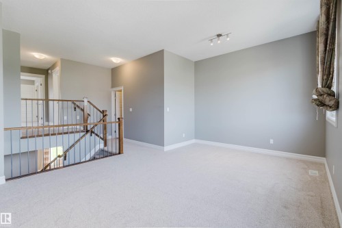 Carpeted flooring, contemporary wall lighting, track lighting fixture, wood and metal staircase railing, and neutral wall tones - 15839 10 Avenue Sw, Edmonton, AB - Indoor Photo Showing Other Room