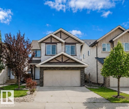 Two-story residential structure featuring a stone and siding exterior, an attached garage, a concrete driveway, and a front lawn with established landscaping - 15839 10 Avenue Sw, Edmonton, AB - Outdoor With Facade