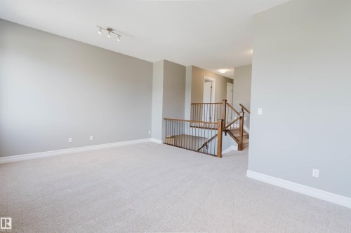 Carpeted open-concept area featuring light gray walls, white trim, track lighting, and a wood and metal staircase - 15839 10 Avenue Sw, Edmonton, AB - Indoor Photo Showing Other Room