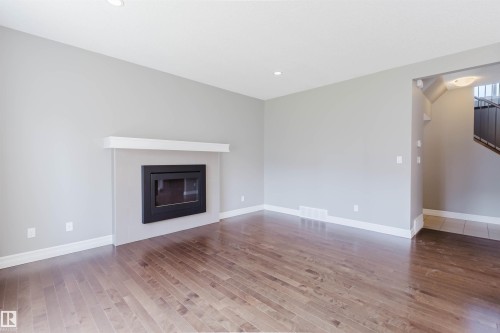Hardwood flooring, recessed lighting, modern fireplace with white mantel, light gray wall finishes, and white baseboards - 15839 10 Avenue Sw, Edmonton, AB - Indoor Photo Showing Living Room With Fireplace