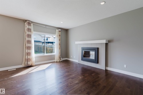Wood-finish flooring, recessed lighting, and a modern fireplace with a tiled surround - 15839 10 Avenue Sw, Edmonton, AB - Indoor Photo Showing Living Room With Fireplace