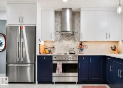 Stainless steel appliances, white upper cabinetry, blue lower cabinetry, white countertops, and a decorative tile backsplash - 