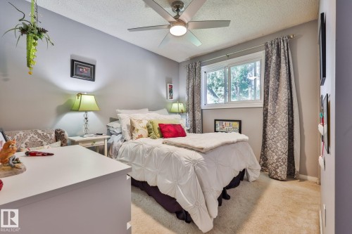 Ceiling fan with integrated lighting, window with white frame, patterned drapes, carpeted flooring, and neutral wall color - 8932 187 Street Nw, Edmonton, AB - Indoor Photo Showing Bedroom