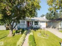 Exterior featuring a light-colored facade, a prominent bay window, a red entry door, a paved driveway, and a front yard with mature landscaping - 8932 187 Street Nw, Edmonton, AB  - Outdoor 
