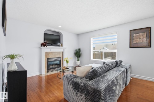 Hardwood flooring, fireplace with stone surround, built-in media niche, white trim, and a large window - 3016 24 Ave Nw, Edmonton, AB - Indoor Photo Showing Living Room With Fireplace