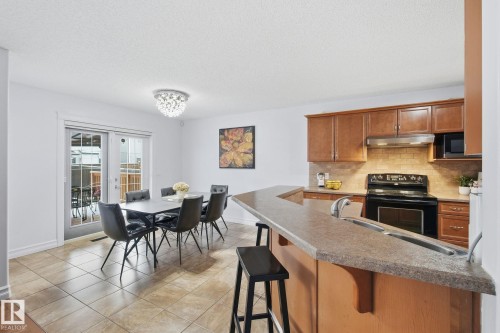 Open-concept kitchen and dining area featuring wood cabinetry, a tiled backsplash, and an integrated breakfast bar - 3016 24 Ave Nw, Edmonton, AB - Indoor