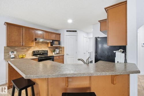 Kitchen featuring wood-finish cabinetry, a breakfast bar, stone-look countertops, and a tile backsplash - 3016 24 Ave Nw, Edmonton, AB - Indoor Photo Showing Kitchen