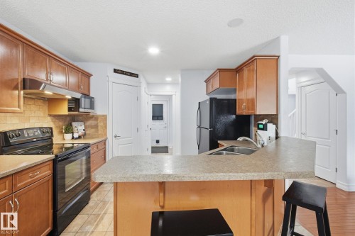 Kitchen featuring wood cabinetry, stone-finish countertops, tile backsplash, and a breakfast bar with a double basin sink - 3016 24 Ave Nw, Edmonton, AB - Indoor Photo Showing Kitchen With Double Sink