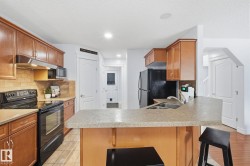 Kitchen featuring wood cabinetry, stone-finish countertops, tile backsplash, and a breakfast bar with a double basin sink - 