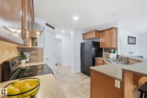 Kitchen featuring wood cabinetry, stone countertops, stainless steel sink, black appliances, and tiled flooring - 3016 24 Ave Nw, Edmonton, AB - Indoor Photo Showing Kitchen With Double Sink