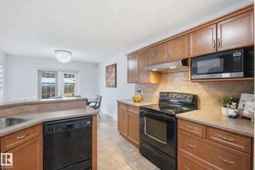 Wood-finish cabinetry, tile flooring, stone-finish countertops, stainless steel sink, and a tile backsplash - 3016 24 Ave Nw, Edmonton, AB - Indoor Photo Showing Kitchen