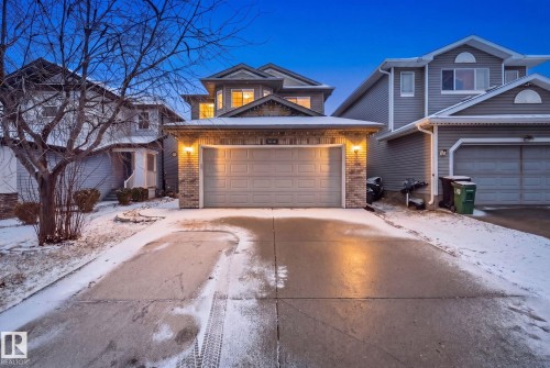 Exterior featuring a two-story design, a prominent attached garage with a panel door, brick accents, and a concrete driveway - 3016 24 Ave Nw, Edmonton, AB - Outdoor With Facade