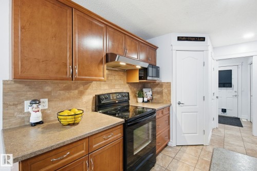 Kitchen featuring wood-finish cabinetry, tile backsplash, built-in microwave, and a black electric range with an overhead exhaust fan - 3016 24 Ave Nw, Edmonton, AB - Indoor Photo Showing Kitchen