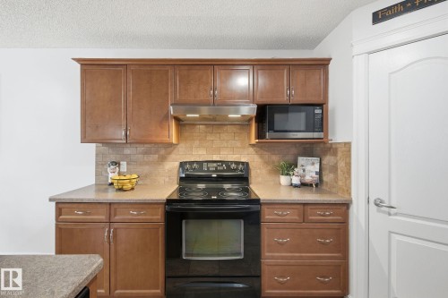 Kitchen featuring rich wood cabinetry, integrated microwave, black electric range, and a tiled backsplash - 3016 24 Ave Nw, Edmonton, AB - Indoor Photo Showing Kitchen