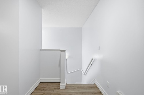 Wood-finish flooring leading to a staircase with white handrails and a white newel post - 3016 24 Ave Nw, Edmonton, AB - Indoor Photo Showing Other Room