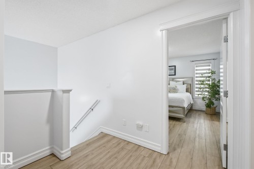 Light wood-finish flooring with white baseboards and trim, featuring a hallway opening into a room with a window - 3016 24 Ave Nw, Edmonton, AB - Indoor Photo Showing Other Room