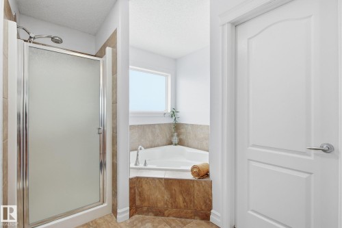 Corner soaking tub with tile surround, separate shower with frosted glass enclosure, and tiled flooring - 3016 24 Ave Nw, Edmonton, AB - Indoor Photo Showing Bathroom