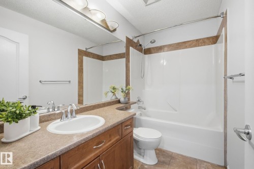 Wood-finish vanity with an integrated sink, broad countertop, full-width mirror, and a combination shower and bathtub - 3016 24 Ave Nw, Edmonton, AB - Indoor Photo Showing Bathroom