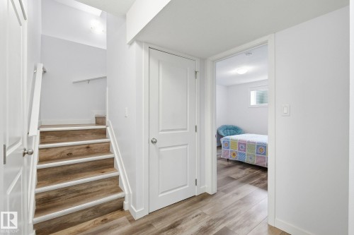 Hardwood-finish flooring throughout, white interior doors, and a wood-finish staircase with white risers - 3016 24 Ave Nw, Edmonton, AB - Indoor Photo Showing Other Room