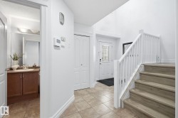 Tiled entryway with wood-finish stairs, white railing, and a front door with decorative glass - 