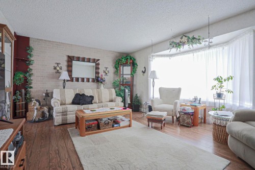 Living area featuring wood-finish flooring, a textured white ceiling, and a prominent bay window - 5203 45 Street, Beaumont, AB - Indoor Photo Showing Living Room