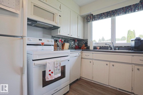 Kitchen featuring white cabinetry, dark countertops, a mosaic tile backsplash, wood-finish flooring, and a large window above the sink - 5203 45 Street, Beaumont, AB - Indoor Photo Showing Kitchen With Double Sink