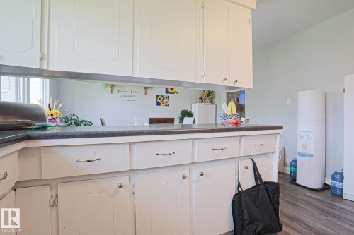 Kitchen featuring white cabinetry with silver hardware, dark countertops, and wood-finish flooring - 5203 45 Street, Beaumont, AB - Indoor