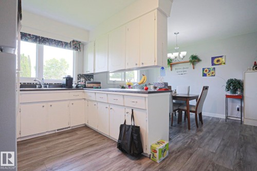 Kitchen featuring white cabinetry, dark countertops, a window over the sink, and wood-finish flooring - 5203 45 Street, Beaumont, AB - Indoor