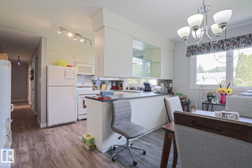 Kitchen and dining area featuring wood-finish flooring, white cabinetry, a dark countertop, and a window with a patterned valance - 5203 45 Street, Beaumont, AB - Indoor Photo Showing Kitchen