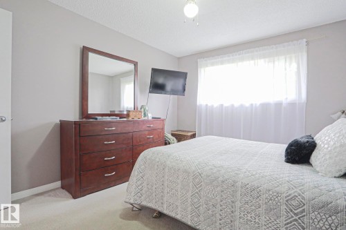Wall-mounted television above a wood-finish dresser with a matching framed mirror - 5203 45 Street, Beaumont, AB - Indoor Photo Showing Bedroom
