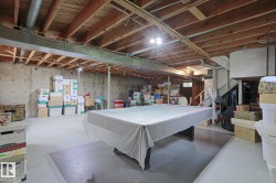 Spacious unfinished basement offering concrete flooring, exposed wood joists, a substantial support beam, and a staircase - 