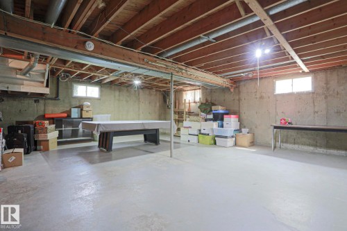 Unfinished basement featuring concrete walls and flooring, exposed wood beam ceiling, and two small windows providing natural light - 5203 45 Street, Beaumont, AB - Indoor Photo Showing Basement