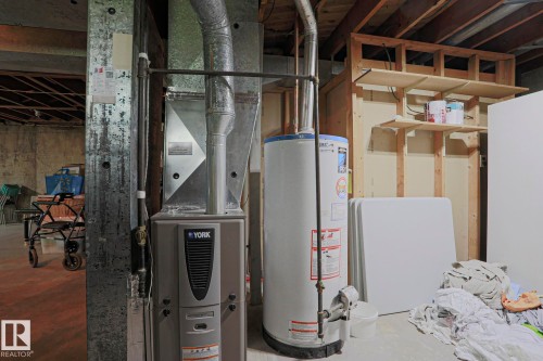 Utility area featuring a water heater, furnace, exposed wood ceiling joists, and built-in wood shelving - 5203 45 Street, Beaumont, AB - Indoor Photo Showing Basement
