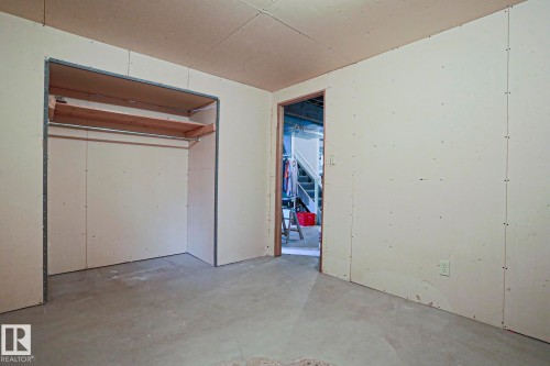 Room featuring exposed drywall, concrete flooring, and an open closet with a metal hanging rod and wood shelving - 5203 45 Street, Beaumont, AB - Indoor Photo Showing Garage