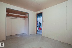 Room featuring exposed drywall, concrete flooring, and an open closet with a metal hanging rod and wood shelving - 